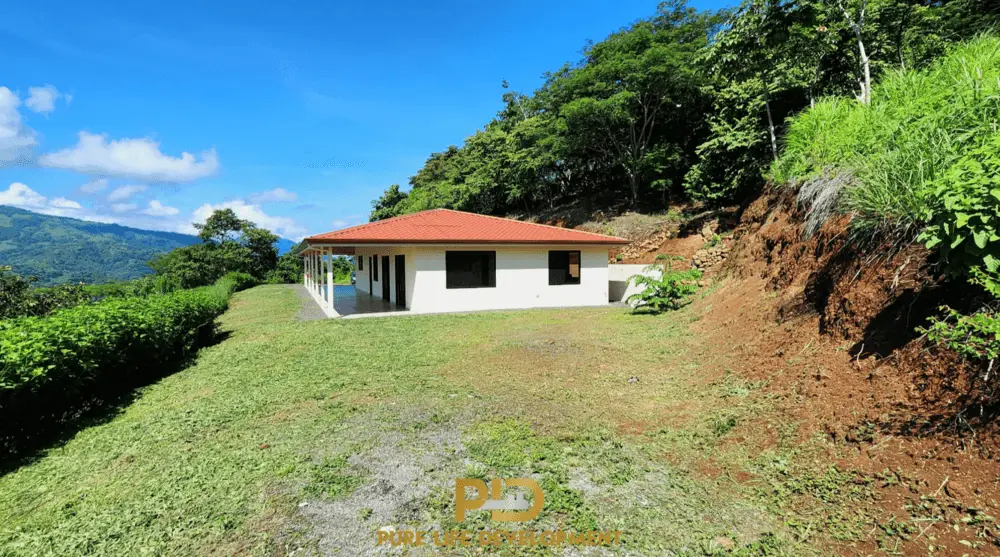 House with red roof in lush green landscape.