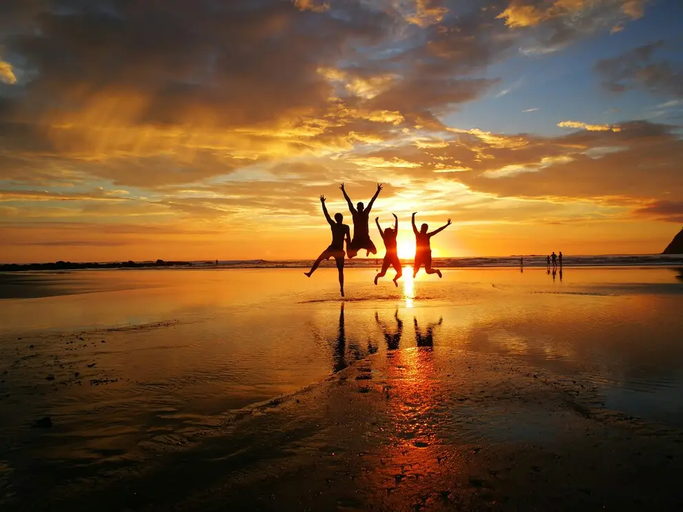 People jumping on beach during sunset.