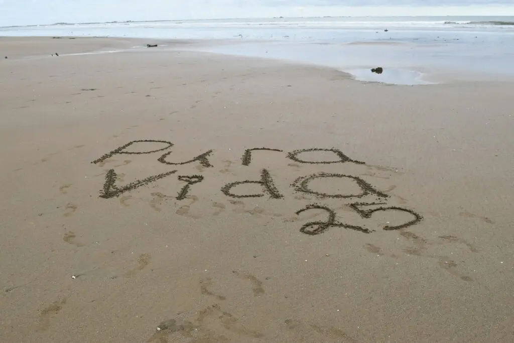 'Pura Vida 2023' written on sandy beach.