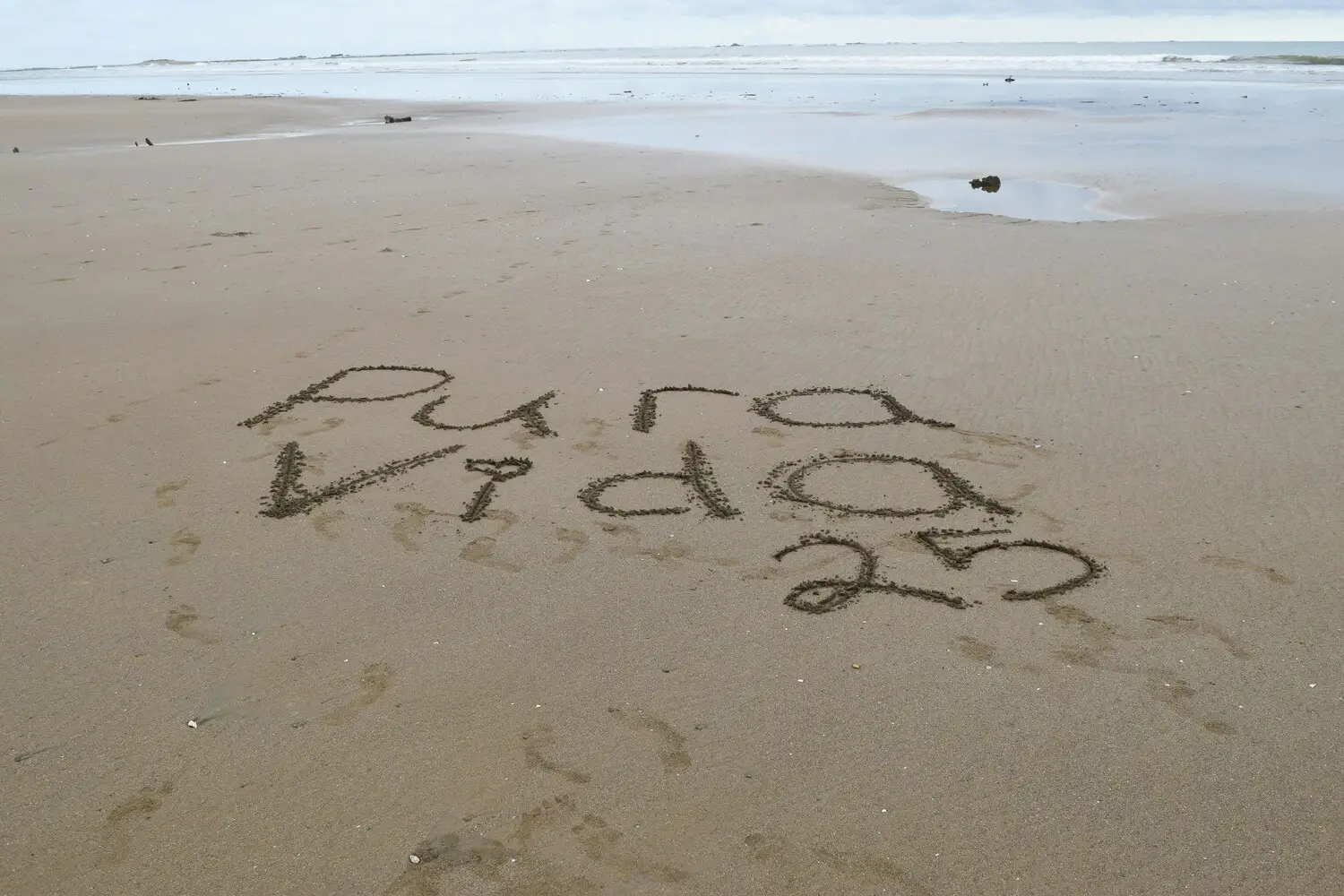 'Pura Vida 2023' written on sandy beach.