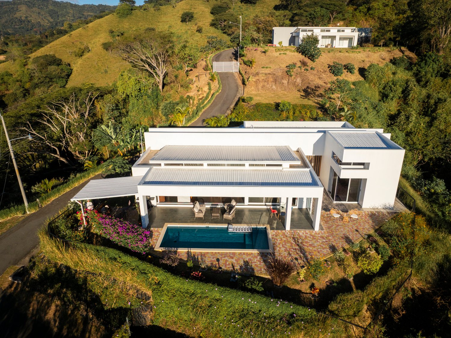 Modern hillside house with pool and lush surroundings.